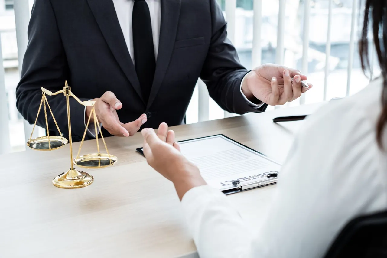 Attorney explaining a document to a client across a desk with scales of justice