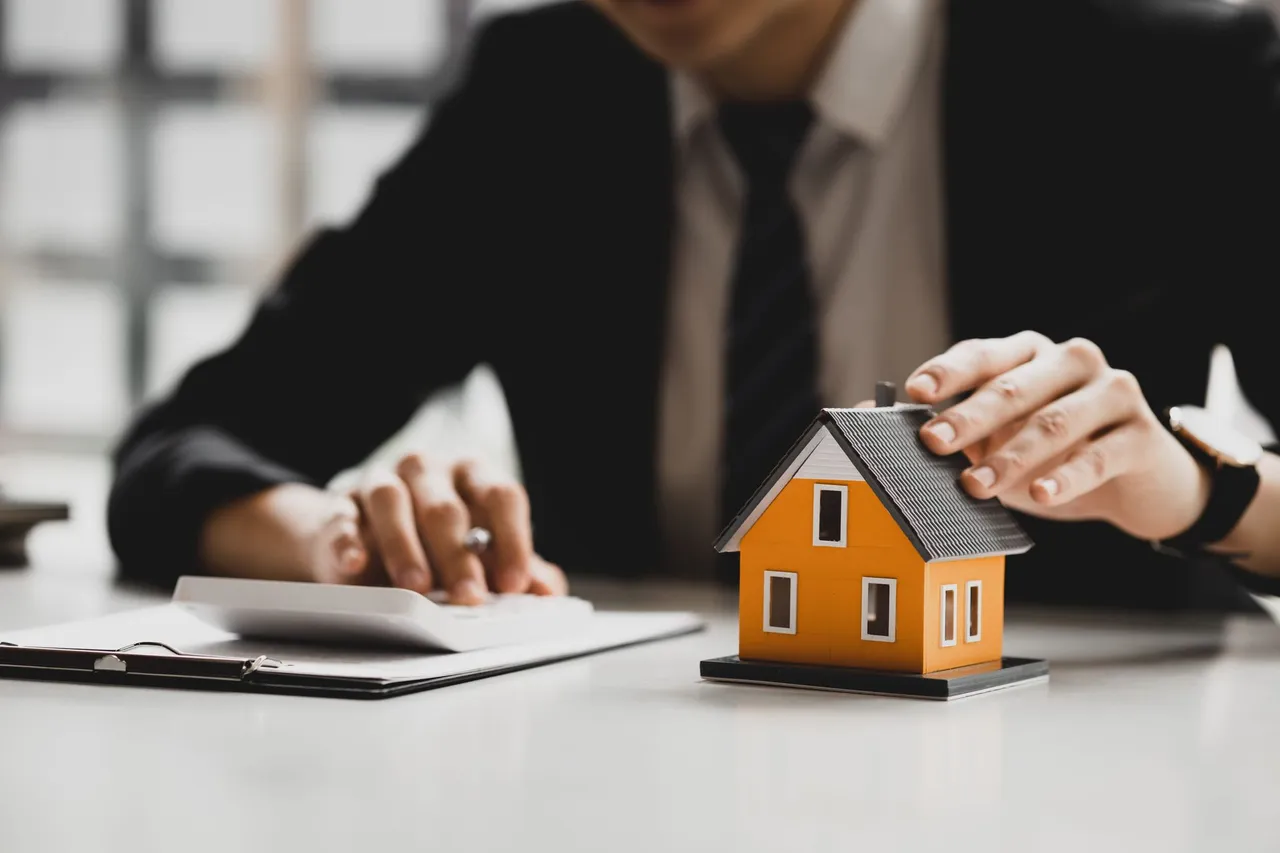 Professional at a desk resting a hand on a small model house beside paperwork