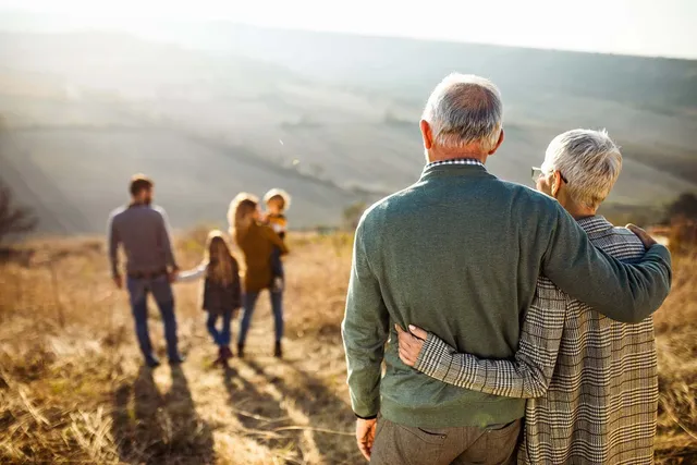 Grandparents walking with their family through a field at sunset